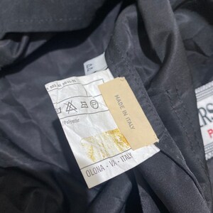 May include: A black jacket with a white label that says "MADE IN ITALY" and "OLONA - VA - ITALY". The label also has a symbol that indicates the jacket is made of polyester.