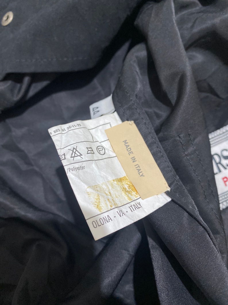 May include: A black jacket with a white label that says "MADE IN ITALY" and "OLONA - VA - ITALY". The label also has a symbol that indicates the jacket is made of polyester.