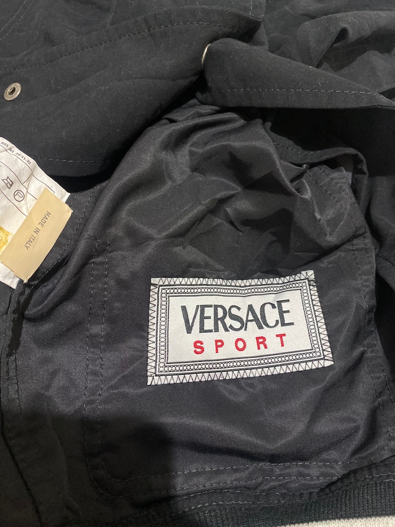 May include: Black jacket with a white and black Versace Sport label on the pocket.