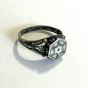 May include: A silver ring with a hexagonal design featuring a star in the center. The ring has a textured band with small dots.