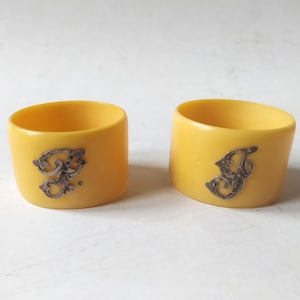May include: Two yellow napkin rings with silver decorative accents. The rings are made of plastic and have a smooth, glossy finish.
