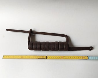 Puede incluir: Una herramienta de metal marrón oxidado con un mango hecho de cilindros apilados. La herramienta tiene un brazo largo y plano que se extiende desde el mango, y una cinta métrica se coloca debajo. La herramienta mide aproximadamente 48 cm de largo.
