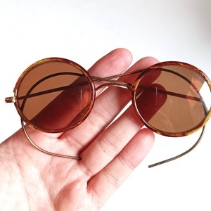 May include: Round tortoiseshell sunglasses with brown lenses and a thin gold metal frame.
