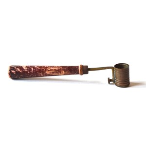 Peut inclure: Un outil vintage en laiton et en bois avec une poignée en bois et un cylindre en laiton avec un petit bouton sur le côté.