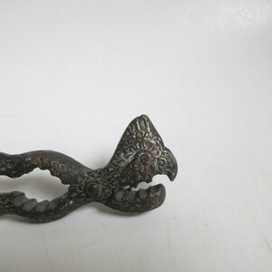 May include: Antique ornate metal nutcracker with a bird head design. The nutcracker is made of dark metal with a green patina.