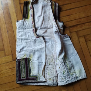 May include: A white sleeveless waistcoat with intricate embroidery in shades of red, green, yellow, and black. The waistcoat has a button closure and is made of a lightweight fabric.