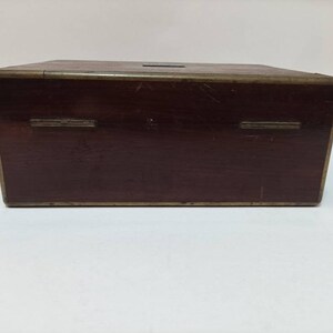 May include: A dark brown wooden box with brass accents. The box has a hinged lid and two brass hinges on the front.