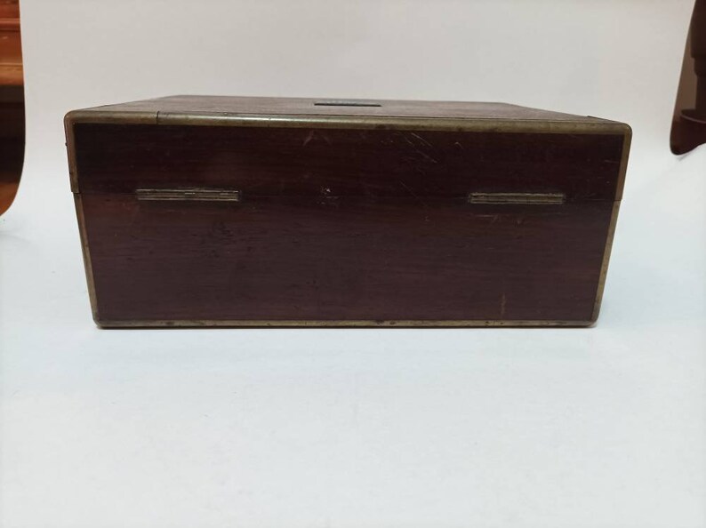 May include: A dark brown wooden box with brass accents. The box has a hinged lid and two brass hinges on the front.