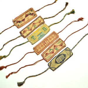 May include: Six colorful embroidered bookmarks with tassels. The bookmarks feature different designs and words, including "LOVE", "TRUST", and "FRIEND".