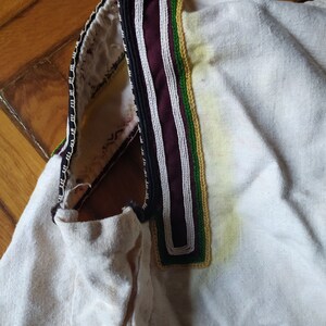 May include: White linen shirt with a black, white and green embroidered collar.