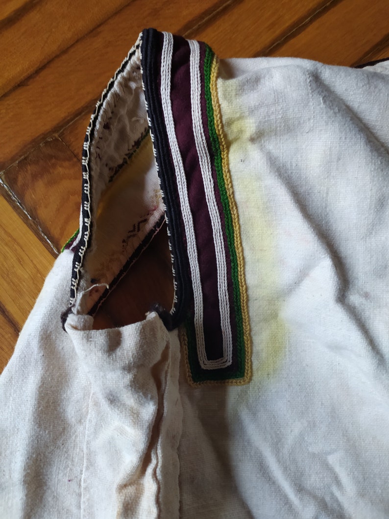 May include: White linen shirt with a black, white and green embroidered collar.