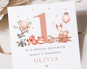 May include: A pink and white card with a woodland animal theme. The card features a large pink number one, a raccoon, a fox, a deer, a squirrel, and a hedgehog. The text on the card reads "To a special daughter Happy 1st Birthday Olivia".