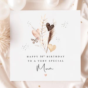 Pode incluir: Cart&atilde;o branco com a mensagem "Happy 50th Birthday to a very special Mum". O cart&atilde;o apresenta um design em aquarela de cora&ccedil;&otilde;es, folhas e uma borboleta em tons de castanho, p&ecirc;ssego e dourado. Elementos decorativos: pequenas esferas brancas.