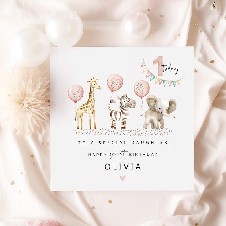 May include: A white greeting card with watercolor illustrations of a giraffe, zebra, and elephant, each holding a pink balloon. The card reads "To a special daughter, Happy first birthday Olivia."