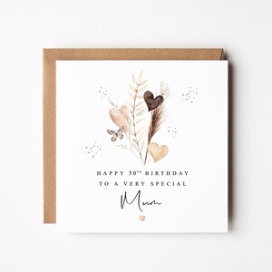 Pode incluir: Um cart&atilde;o de anivers&aacute;rio com uma borda de papel kraft castanho. O cart&atilde;o branco apresenta um desenho em aquarela de cora&ccedil;&otilde;es, borboletas e folhagens em tons neutros. O texto diz "Happy 50th Birthday to a very special Mum."