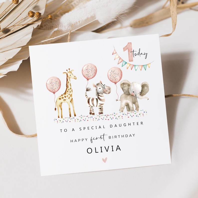 May include: A white birthday card with watercolor illustrations of a giraffe, zebra, and elephant, each holding a pink balloon. The card reads "To a special daughter, Happy first birthday, Olivia."
