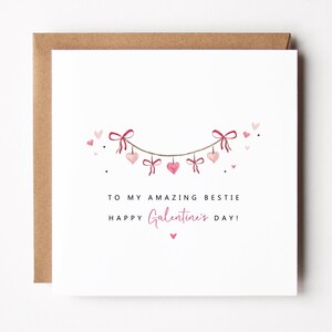 Puede incluir: Tarjeta de felicitaci&oacute;n cuadrada con fondo blanco y sobre marr&oacute;n. La tarjeta presenta una guirnalda de corazones y lazos rosas. El texto dice "TO MY AMAZING BESTIE" y "HAPPY Galentine's DAY!"