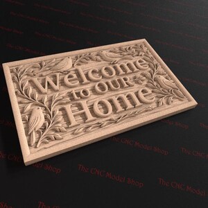 May include: A rectangular wooden sign with the words "Welcome to Our Home" carved into the surface. The sign is decorated with carved birds and foliage. The sign is made of light-colored wood.