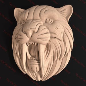 May include: A wooden carving of a saber-toothed tiger's head. The sculpture shows open jaws with large fangs, detailed fur texture, and visible eyes and ears. The piece is likely for decorative purposes.