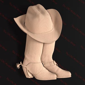 Puede incluir: Un par de botas de vaquero de color marrón claro con espuelas y un sombrero de vaquero de color marrón claro. Las botas tienen una hebilla en el lateral y el sombrero tiene un ala ancha.
