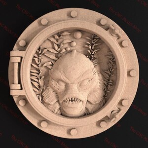 May include: A 3D printed wall decoration featuring a detailed sculpture of the Creature from the Black Lagoon inside a round porthole. The sculpture is made of a light brown material and is set against a dark background.