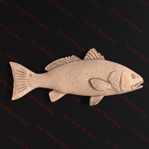 May include: A detailed, light brown wooden carving of a fish, showcasing scales, fins, and a detailed head. The fish is positioned horizontally against a dark background. The CNC Model Shop text is visible.
