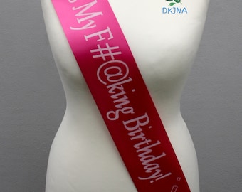 May include: Pink satin sash with the text "It's My F#@king Birthday!" in white lettering and a champagne bottle graphic.