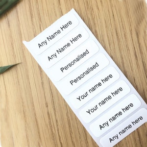May include: A sheet of white rectangular labels with black text. The labels read "Any Name Here", "Personalised", and "Your name here".
