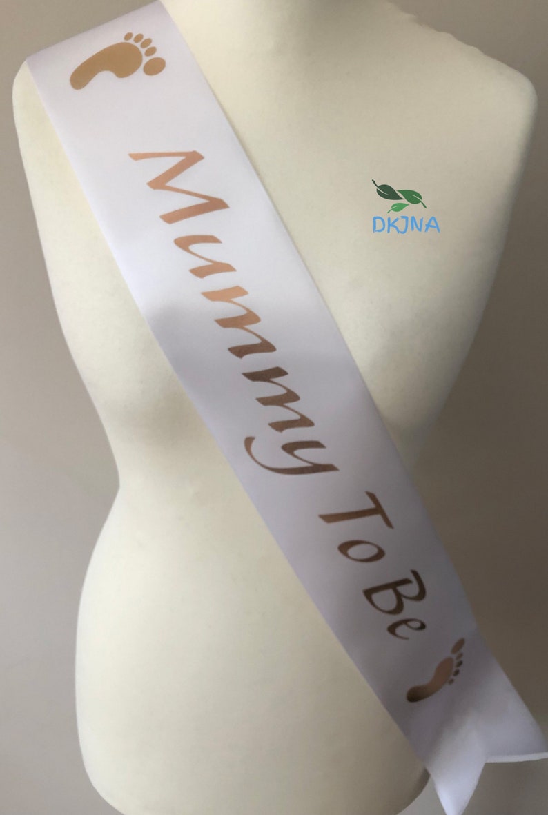 May include: White satin sash with gold foil lettering that reads "Mommy To Be" and gold foil baby footprints on each end.