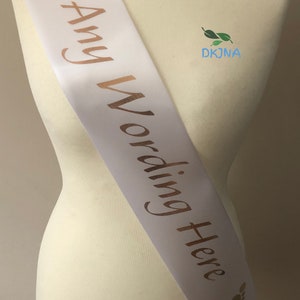 May include: White satin sash with gold foil footprints and the text "Any Wording Here" printed on it.