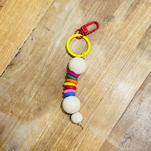 May include: A colorful wooden bead keychain with a yellow ring and a red metal clasp. The beads are white with rainbow colored rings around them.