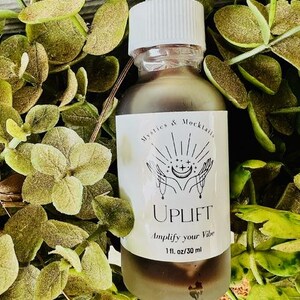 May include: A glass bottle with a white dropper top and a white label. The label says "Mystics & Mocktails" and "UPLIFT Amplify your Vibe 1 fl. oz/30 ml".