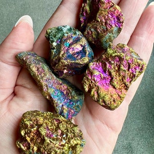 May include: A collection of five iridescent pyrite stones, with a variety of shapes and sizes. The stones have a metallic sheen with shades of gold, purple, and blue.
