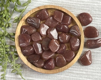 May include: A collection of tumbled rose quartz stones in a wooden bowl. The stones are a light pink color and have a smooth, polished finish.