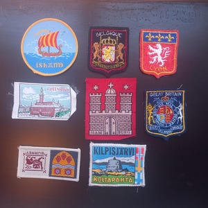 May include: A selection of embroidered patches with diverse designs and text. Includes a Viking ship on a blue background with "ISLAND", a shield with "BELGIQUE", and a red patch with "LYON". Other patches depict cityscapes and heraldic symbols.