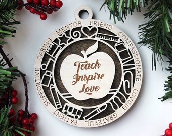May include: Wooden ornament with a brown apple design and the words "Teach Inspire Love" inside. The apple is surrounded by a circle of words including "Caring", "Mentor", "Friend", "Compassionate", "Loving", "Grateful", "Patient", and "Supportive".