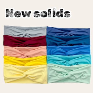May include: A stack of ten colorful fabric headbands in various solid colors, including light blue, dark blue, red, pink, yellow, and light green. The headbands are all twisted into a knot in the center.