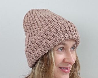 Pode incluir: Um gorro de malha rosa macio com textura canelada. O gorro é usado por uma pessoa com cabelo comprido e castanho claro.