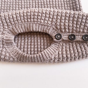 A crew neck opening of a children’s crochet sweater. The neckline is made with a knit-like ribbing made with a yarn over slip stitch with a shoulder button opening with three buttons for an easy baby dressing / undressing.