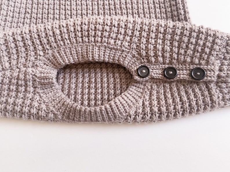 A crew neck opening of a children’s crochet sweater. The neckline is made with a knit-like ribbing made with a yarn over slip stitch with a shoulder button opening with three buttons for an easy baby dressing / undressing.