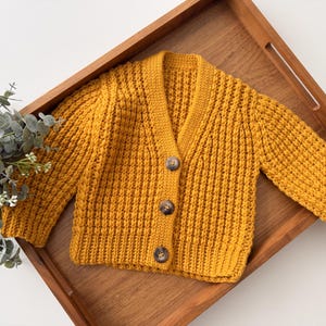 Peut inclure: Un cardigan en tricot jaune avec une fermeture boutonnée. Le cardigan est fait d'un fil doux et texturé et a un design classique.