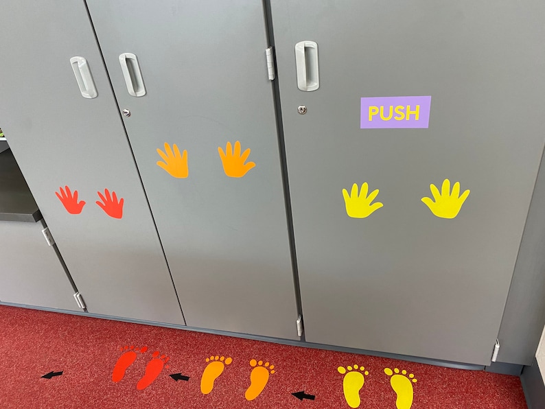 Op de afbeelding: Een grijze kast met hand- en voetgrafieken in geel, oranje en rood. Het woord "PUSH" staat op een paars label. Pijlen en voetafdrukken staan op de rode vloer en geven een pad aan.