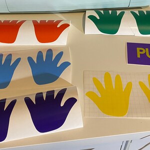 Op de afbeelding: Verschillende kleurrijke handvormige vinylstickers in rood, groen, blauw, geel en paars. Er is ook een paarse rechthoek met het woord "PUSH" in geel. Deze stickers zijn waarschijnlijk voor decoratie of bewegwijzering.