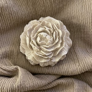 Könnte beinhalten: Eine weiße Keramikblume mit einem detaillierten, strukturierten Design. Die Blume ist eine einzelne Blüte mit mehreren Blütenblattschichten.