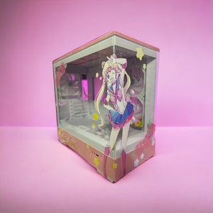 May include: A computer case featuring a Sailor Moon anime design. The case has a clear front panel with a colorful illustration of the character. The case is decorated with pink roses and stars, set against a pink background.