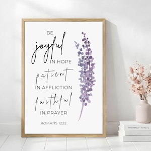 May include: A framed wall art print featuring the text BE joyful IN HOPE patient IN AFFLICTION faithful IN PRAYER ROMANS 12:12 in black lettering alongside a vertical watercolor illustration of purple lavender flowers on a white background.