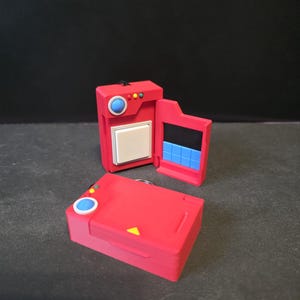 May include: Two red, toy-like cases with hinged doors and button details. One case is open, revealing a black interior with blue blocks. The other case is closed. Both have a blue circle button and a yellow triangle.
