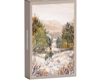 May include: A rectangular box with the word "HOMECOMING" printed vertically on the side. The box features a winter landscape illustration with a person walking through a snowy path, carrying a bundle of greenery. The color palette includes muted tones of beige, green, and brown.