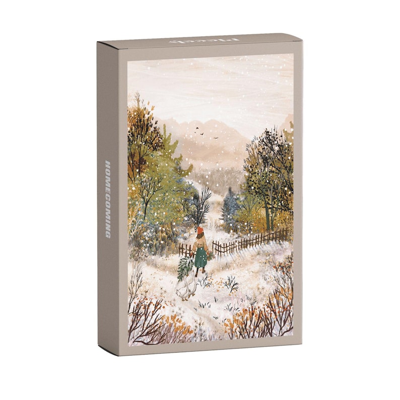 May include: A rectangular box with the word "HOMECOMING" printed vertically on the side. The box features a winter landscape illustration with a person walking through a snowy path, carrying a bundle of greenery. The colour palette includes muted tones of beige, green, and brown.
