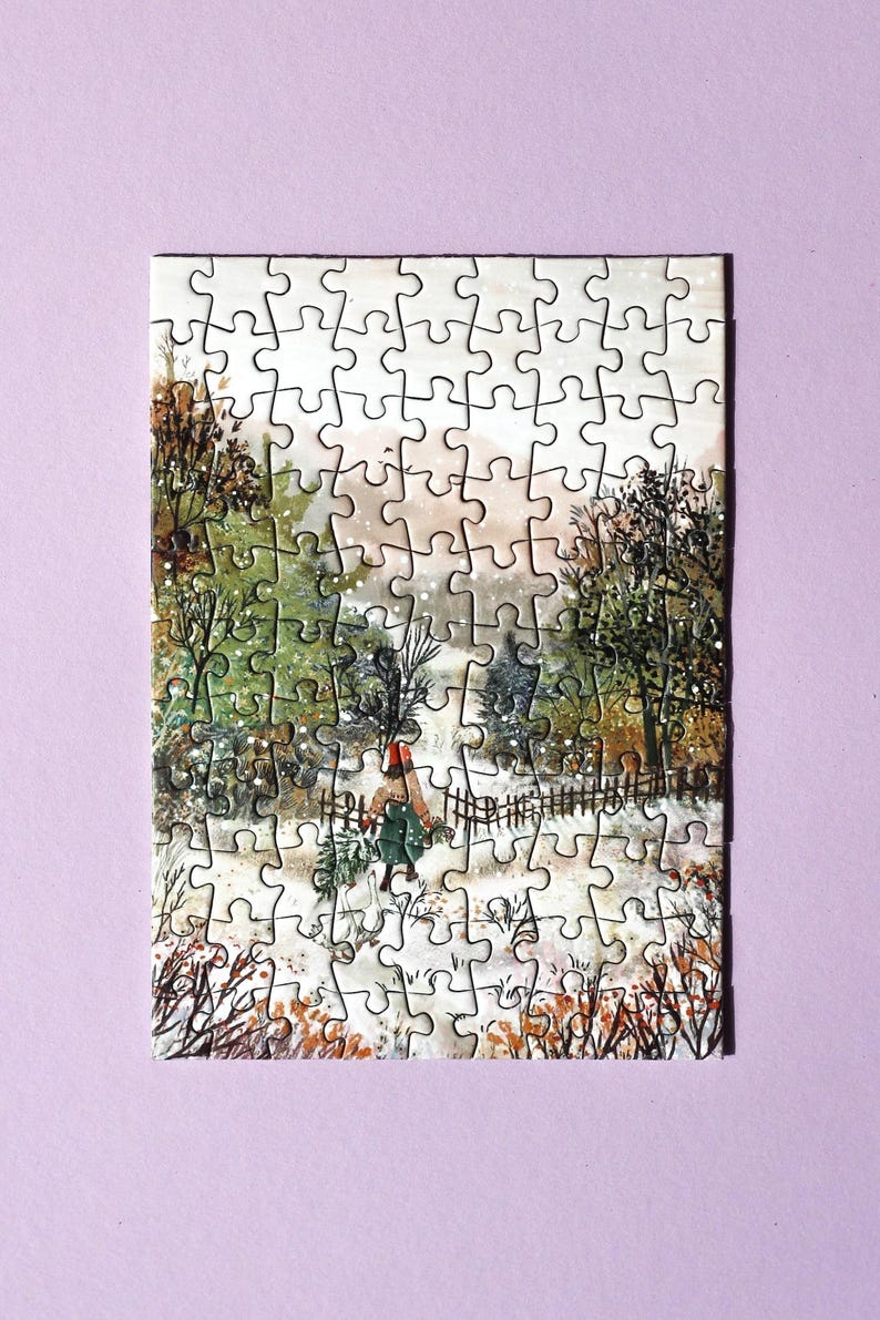 May include: A completed jigsaw puzzle showing a winter landscape. The image features a person walking through snow, carrying branches. The puzzle includes a fence, trees, and a muted colour palette of greens, browns, and whites.